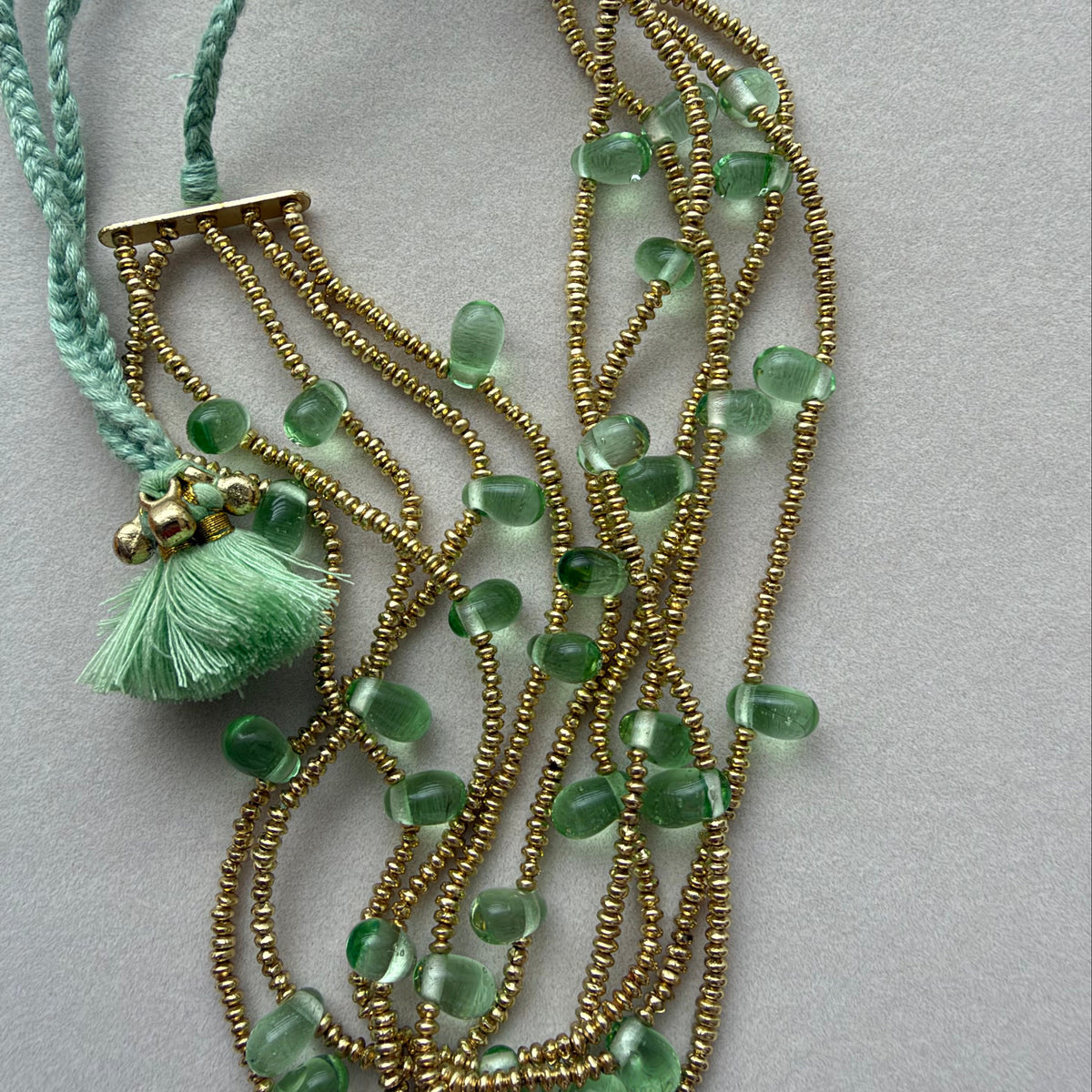 Detalle del collar Ayra menta con pequeñas cuentas doradas, cuentas verdes y cordón con borla menta