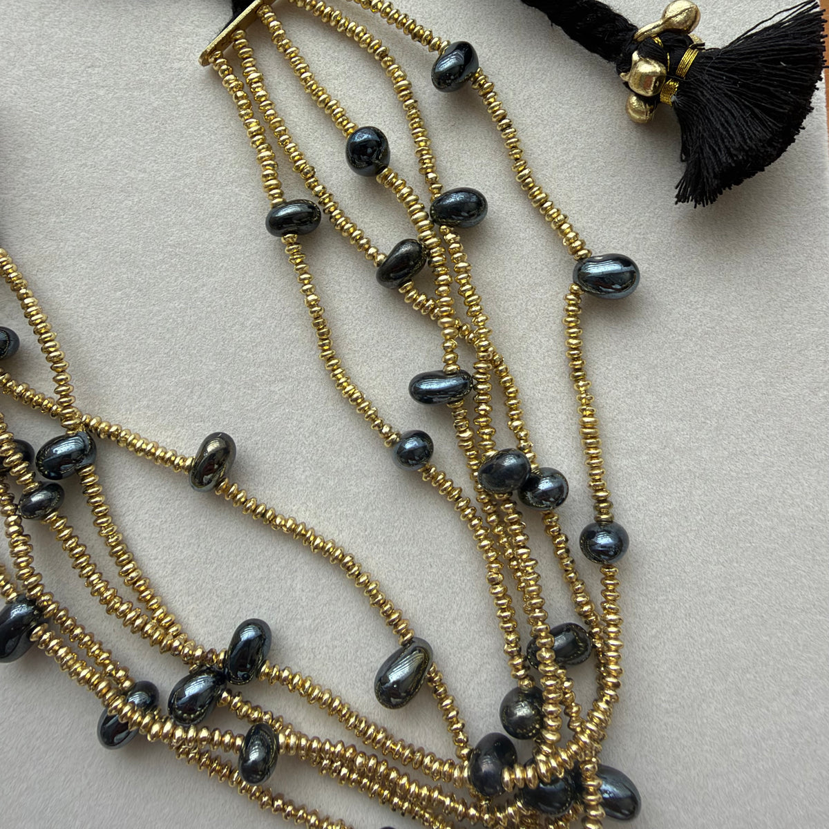 Detalle del collar Ayra negro con pequeñas cuentas doradas, cuentas negras y borla negra