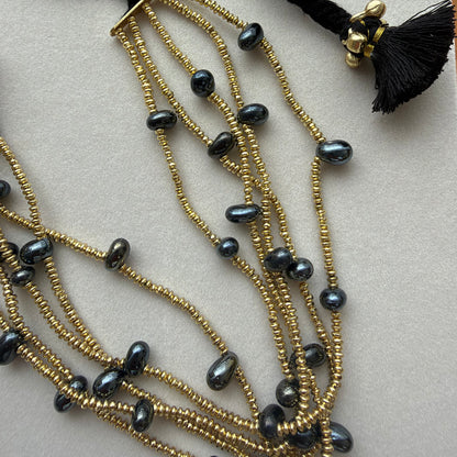 Detalle del collar Ayra negro con pequeñas cuentas doradas, cuentas negras y borla negra