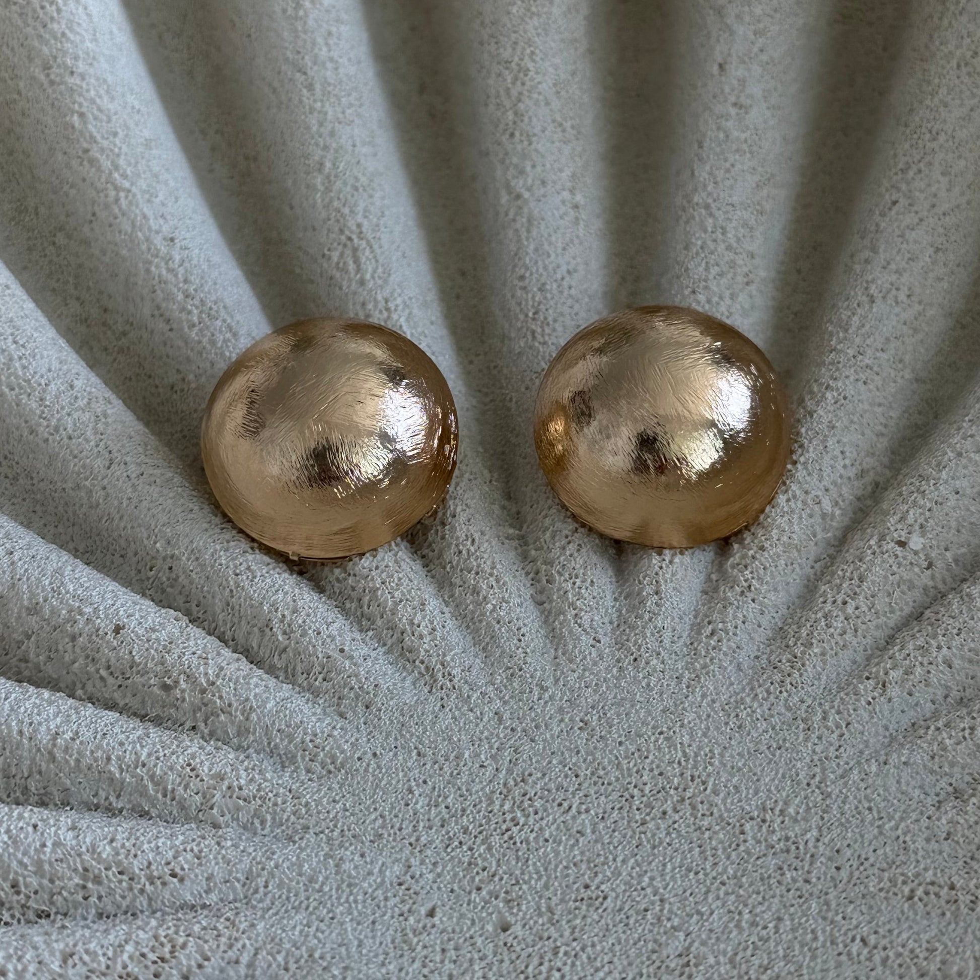 Aros Amelia tipo botón con baño de oro de 18 quilates, hechos en Brasil. Diseño redondo satinado de 2 cm, elegante y liviano.