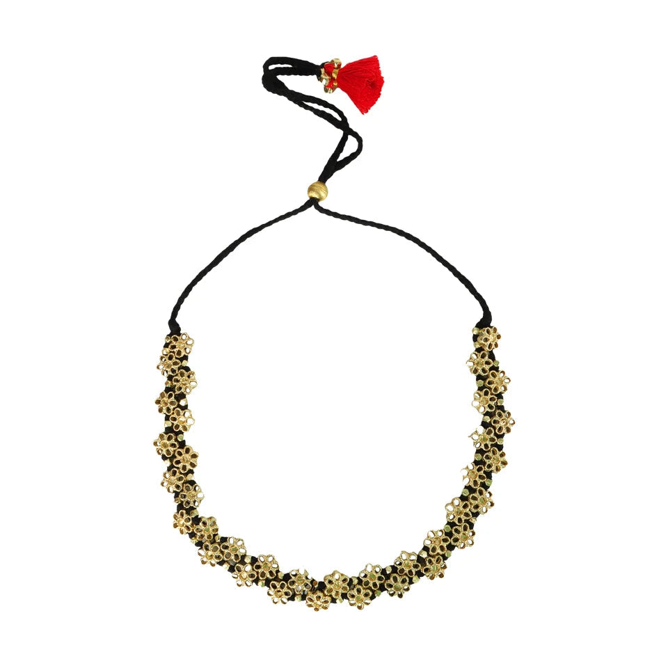 Collar Mishika dorado con flores de espejo, cordón negro ajustable y borla roja sobre fondo blanco.