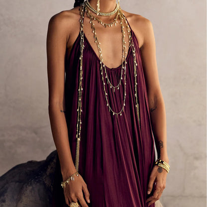 Modelo con pulsera Nayra Dorada en la muñeca y collares y aros dorados sobre un vestido burdeos.