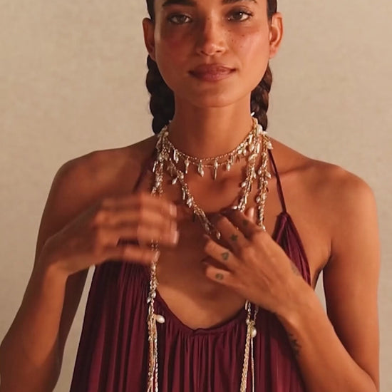 Modelo con pulsera Nayra Dorada en la muñeca y collares y aros dorados sobre un vestido burdeos. Muestra la coleccion Nayra 