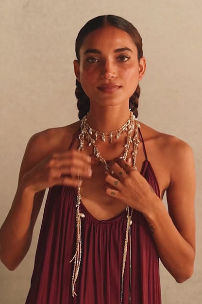 Modelo con pulsera Nayra Dorada en la muñeca y collares y aros dorados sobre un vestido burdeos. Muestra la coleccion Nayra 
